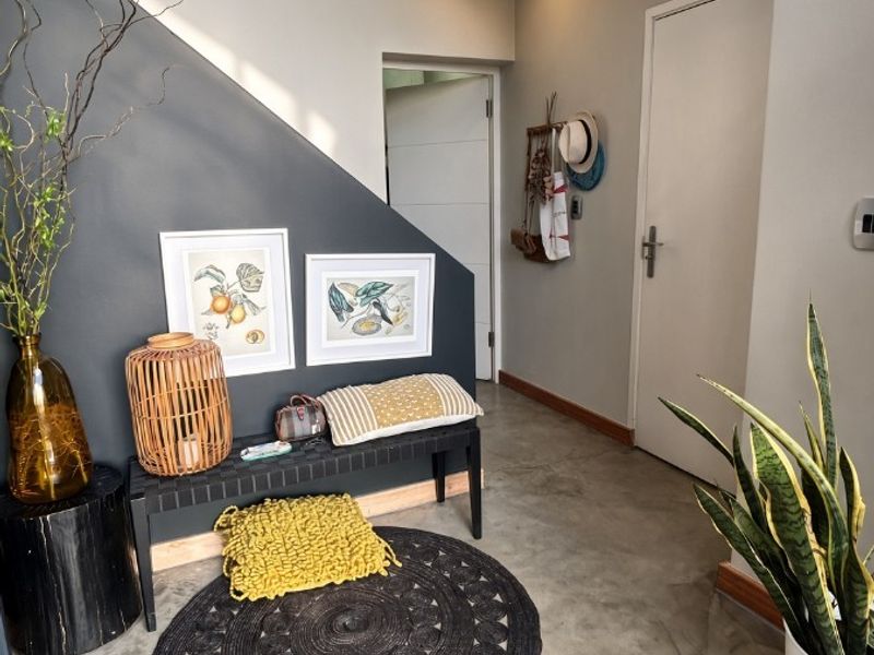 A modern entrance hall featuring polished concrete floors, a striking dark accent wall under the staircase, and clean architectural lines.