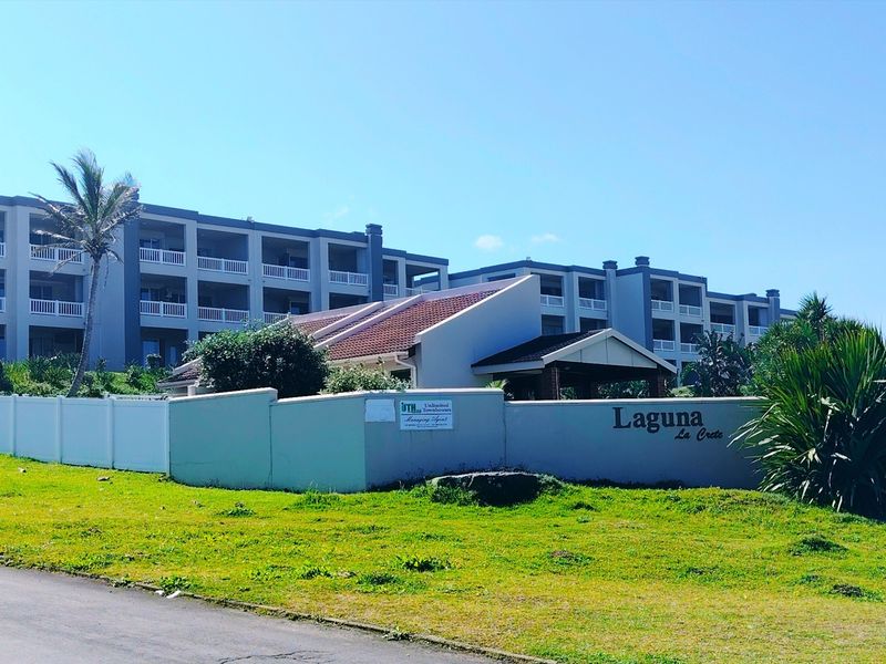 Front exterior view of the Laguna La Crete apartment complex, featuring multi-story residential buildings with balconies and a perimeter boundary wall.