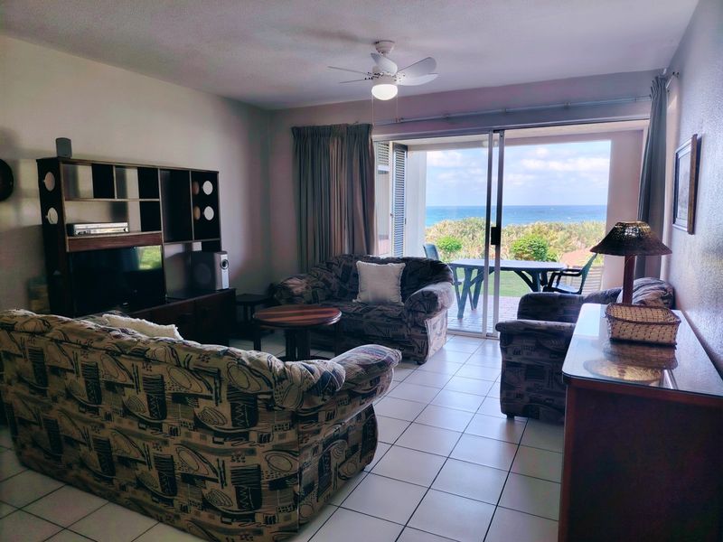 Spacious living room featuring tiled flooring, a ceiling fan, and large sliding glass doors that open to a balcony with ocean views.