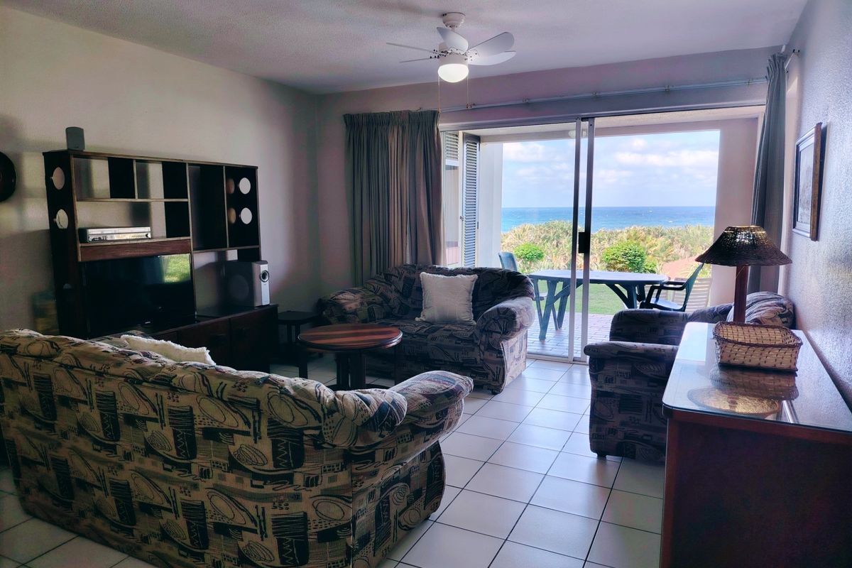 Spacious living room featuring tiled flooring, a ceiling fan, and large sliding glass doors that open to a balcony with ocean views.