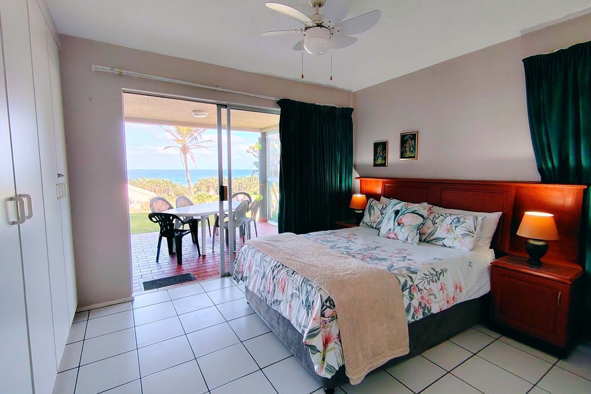 Spacious bedroom featuring tiled flooring, built-in cupboards, a ceiling fan, and direct access to a private patio with ocean views.