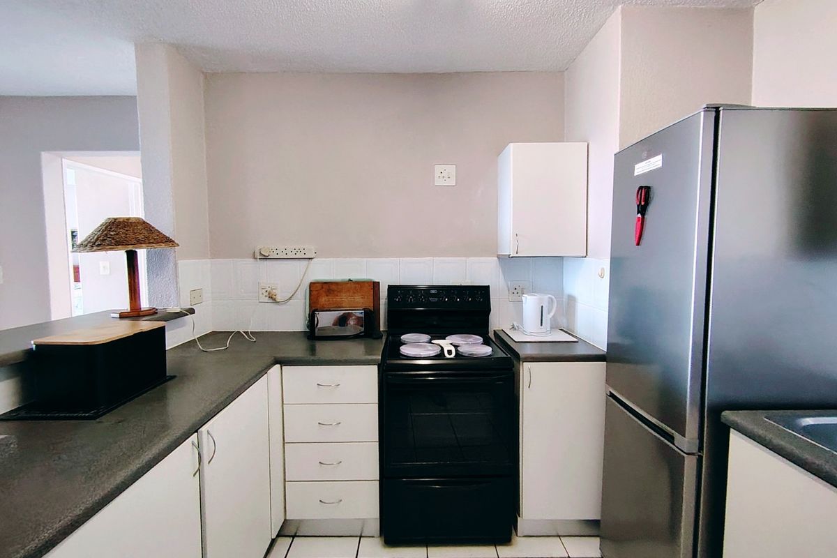 Compact kitchen featuring white cabinetry, dark laminate countertops, tiled backsplash, and a freestanding stove, offering a functional layout for an apartment.