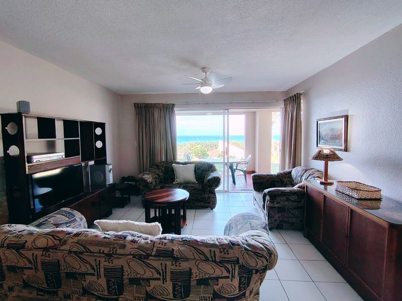 A living room featuring tiled flooring, a ceiling fan, and large sliding glass doors that open to a balcony with ocean views.