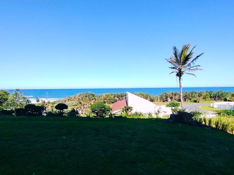 A scenic outdoor view featuring a well-maintained lawn, lush coastal vegetation, and a clear perspective of the ocean horizon.