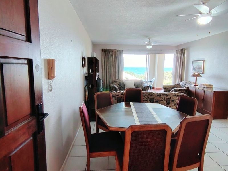 Open plan living and dining area featuring tiled flooring, ceiling fans, and sliding glass doors leading to a balcony with ocean views.