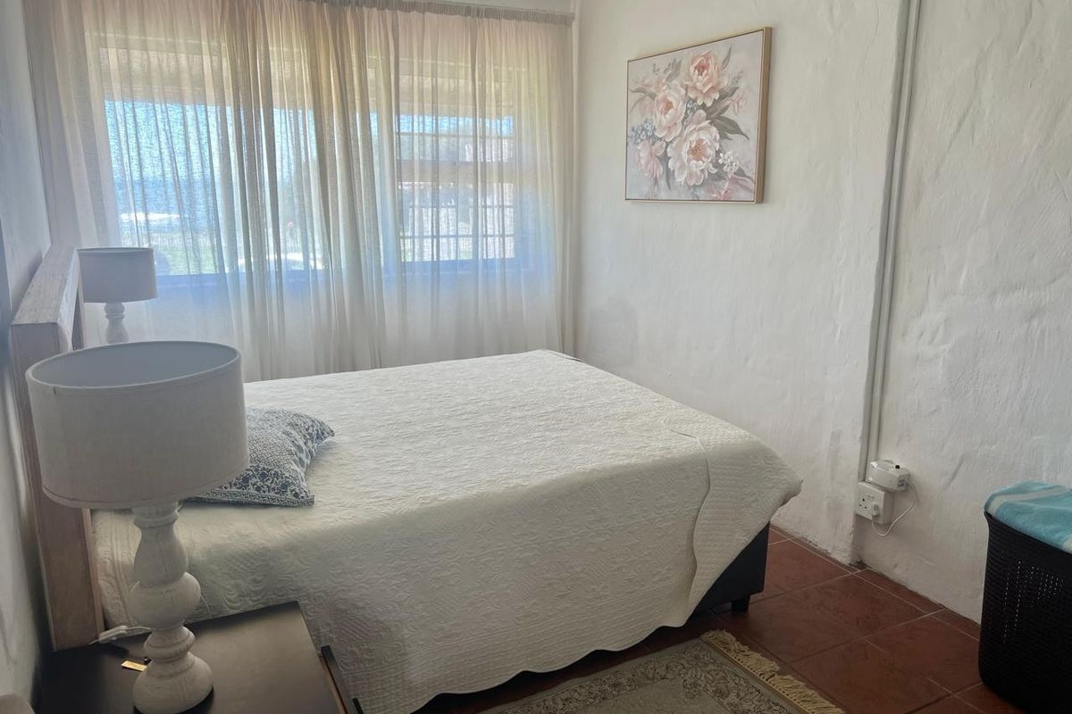 A bedroom featuring textured white walls and terracotta floor tiles, offering a neutral base with natural light through large window curtains.