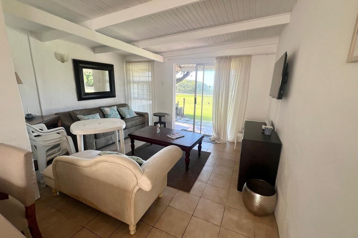 A living room featuring tiled flooring, exposed beam ceilings, and a sliding glass door providing access to the outdoor area.
