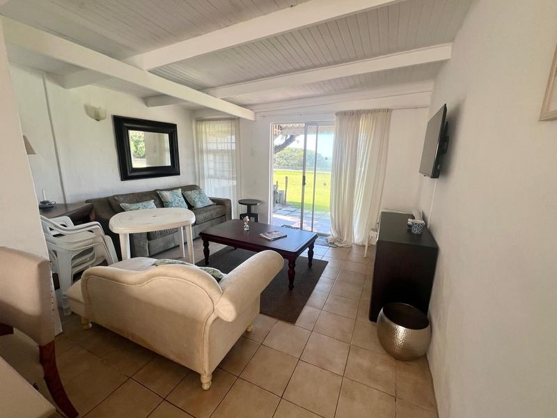 A living room featuring tiled flooring, exposed beam ceilings, and a sliding glass door providing access to the outdoor area.