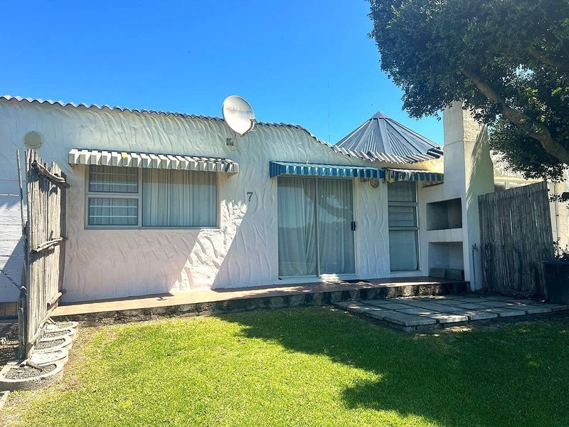 Rear exterior view of the house featuring a tiled patio, built-in braai, sliding glass doors, and a small garden area.