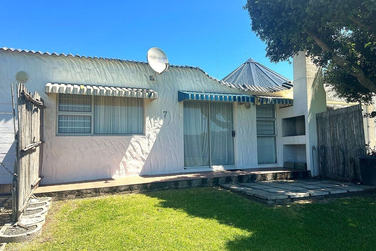 Rear exterior view of the house featuring a tiled patio, built-in braai, sliding glass doors, and a small garden area.
