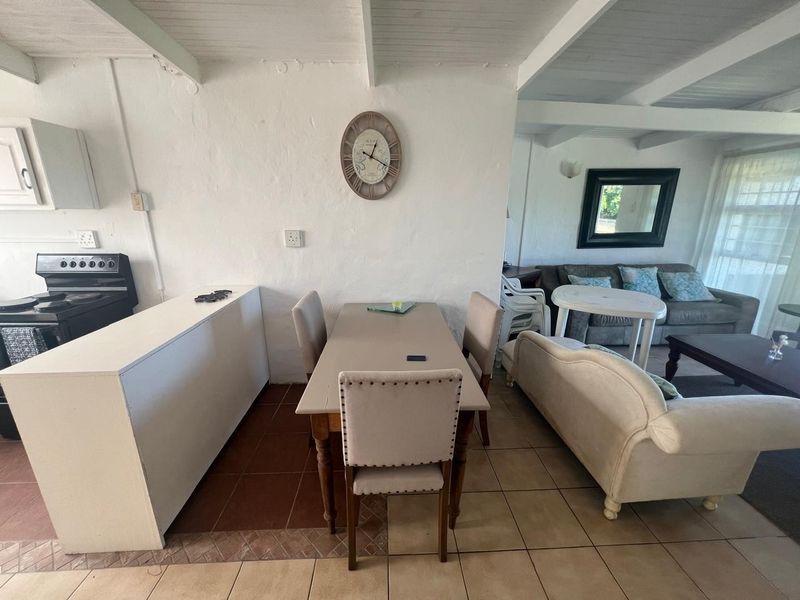 Open-plan living and dining area featuring exposed beam ceilings, tiled flooring, and a compact kitchen space with built-in stove.