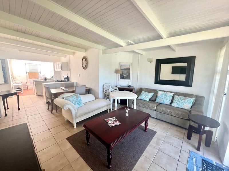Open-plan living and dining area featuring exposed beam ceilings and tiled flooring, seamlessly flowing into the adjacent kitchen space.