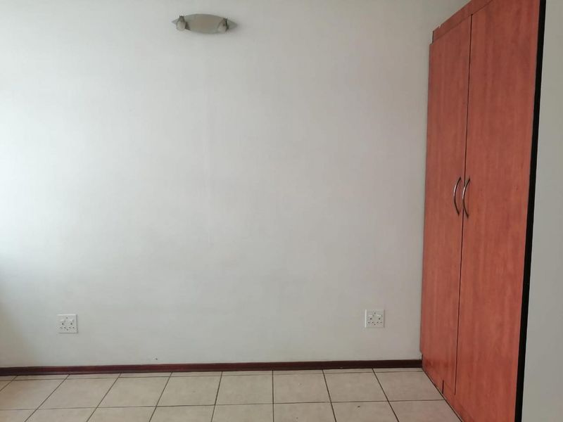 A clean, empty bedroom featuring tiled flooring, a built-in wooden wardrobe, and wall-mounted lighting.