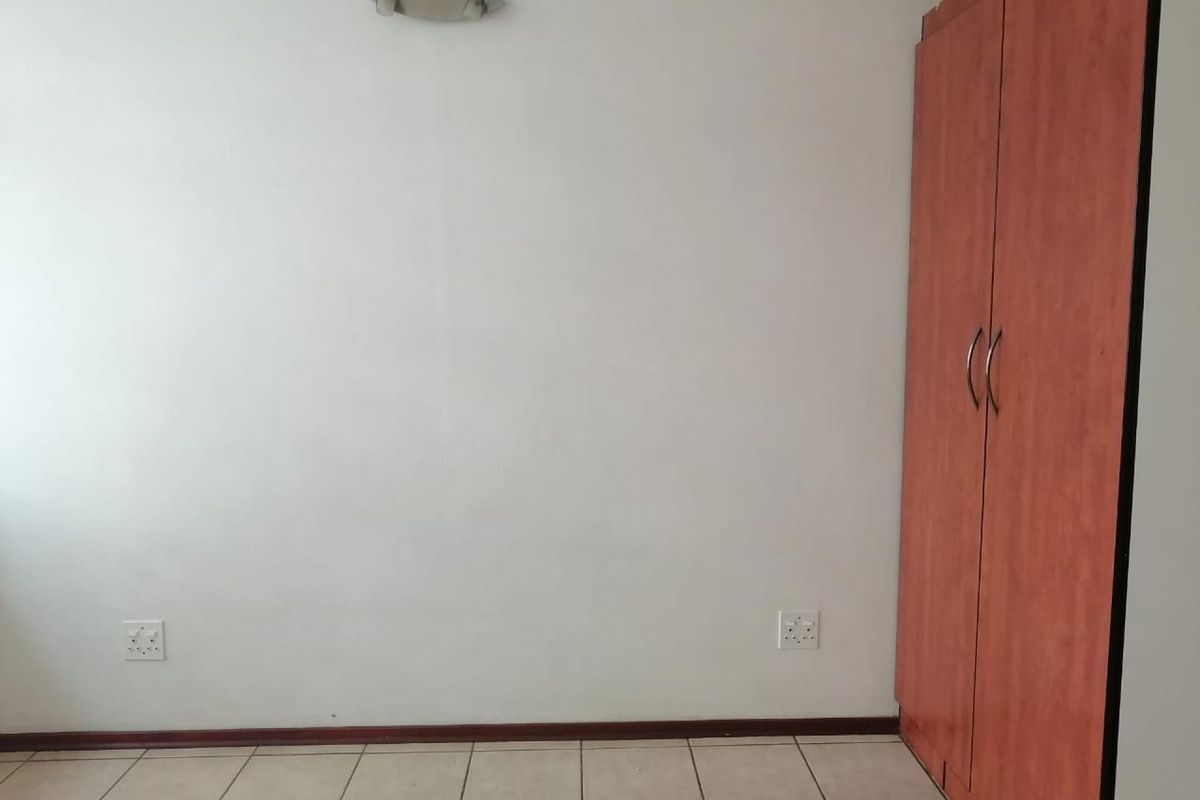 A clean, empty bedroom featuring tiled flooring, a built-in wooden wardrobe, and wall-mounted lighting.
