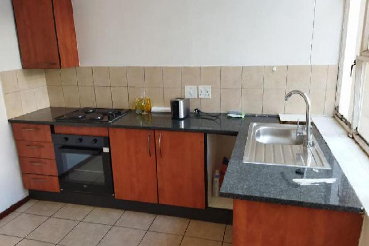 A functional kitchen featuring granite countertops, built-in oven, gas hob, and tiled finishes, offering a practical layout with potential for cosmetic updates.