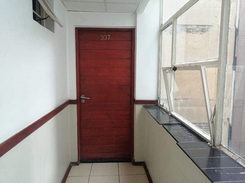 A private apartment entrance featuring a timber door, tiled flooring, and large casement windows overlooking the building exterior.