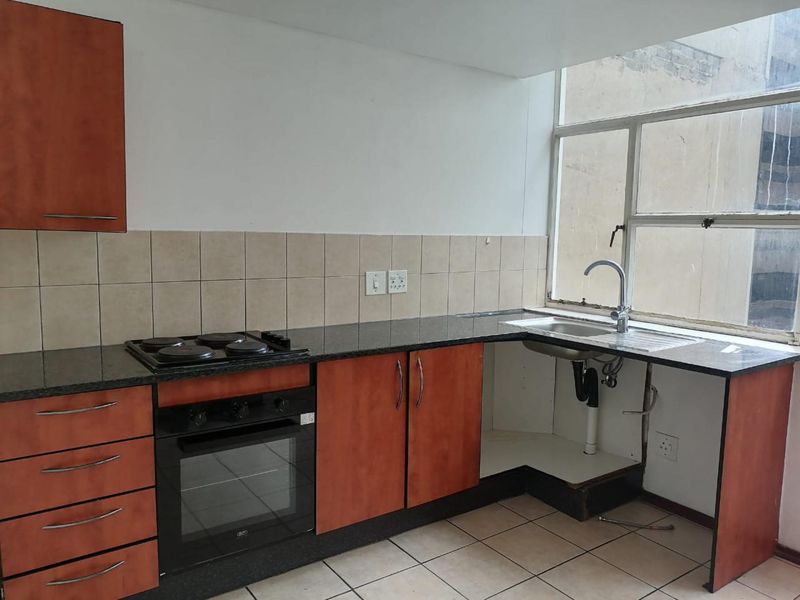 A functional kitchen featuring built-in cabinetry, granite countertops, an electric hob, and an oven, with some maintenance required for the under-sink area.