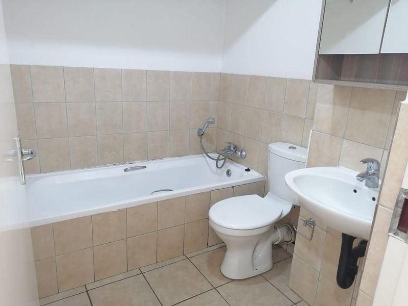 A functional bathroom featuring a bathtub, toilet, and pedestal basin with neutral ceramic tiling throughout.