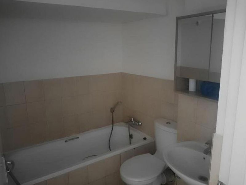 A functional bathroom featuring a bathtub with handheld shower, pedestal sink, toilet, and wall-mounted medicine cabinet with neutral tiled splashback.