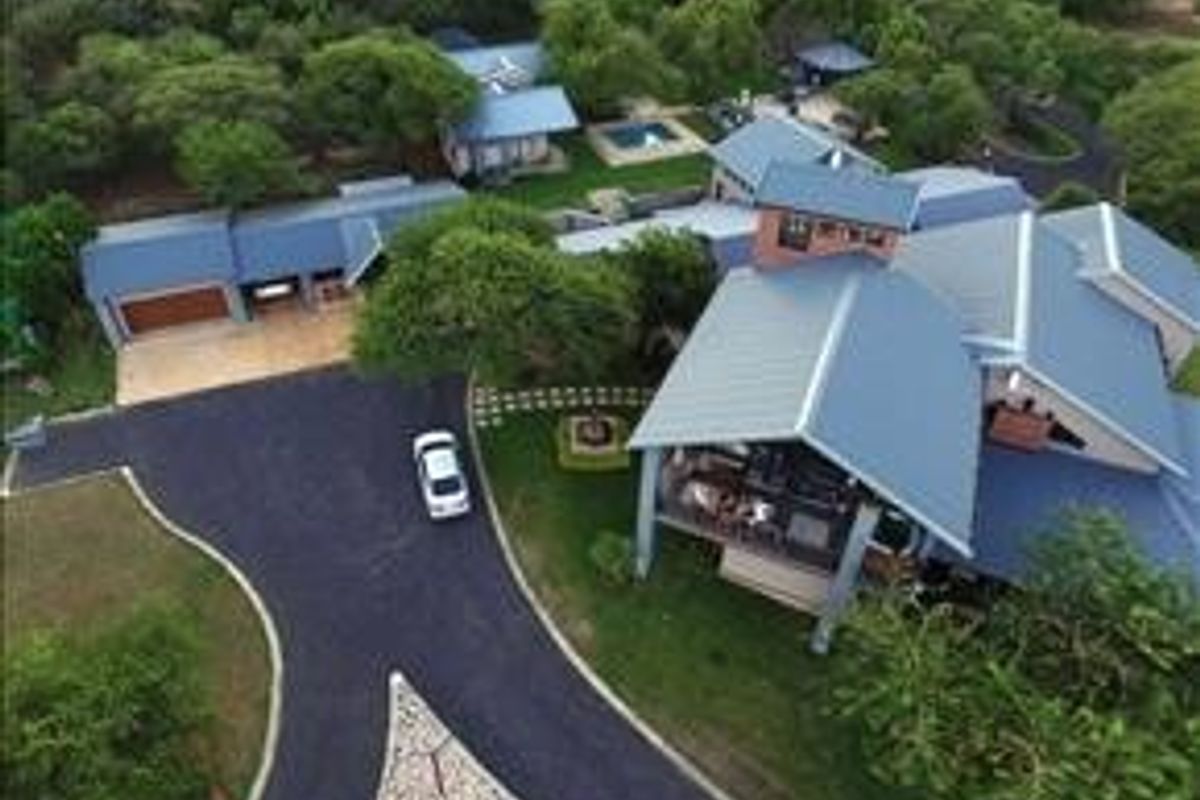 Aerial view of a large farm property featuring multiple buildings, a swimming pool, extensive metal roofing, and a paved driveway.