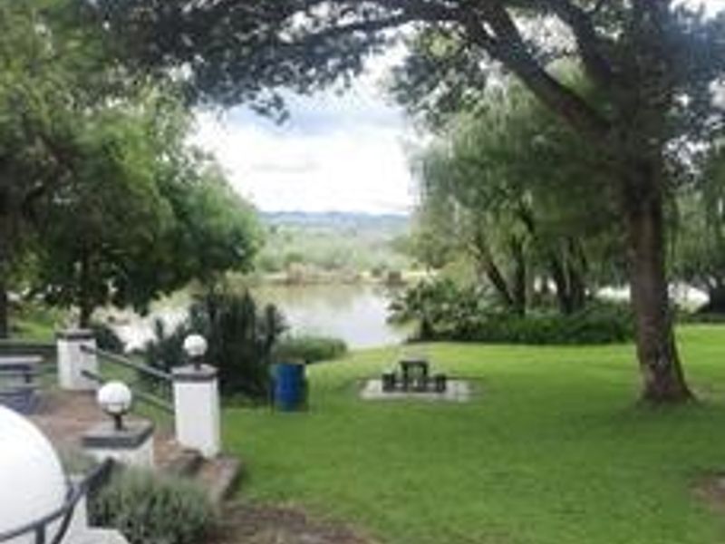 A scenic view of the farm landscape featuring a well-maintained lawn, mature trees, and stone pillar lighting overlooking a tranquil dam.