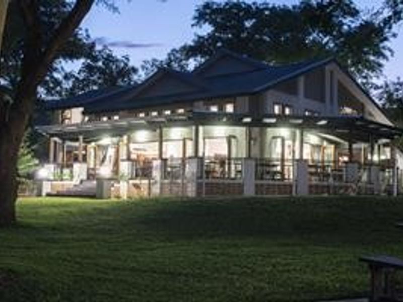 A well-lit rear view of the farm property featuring a spacious covered patio, large glass doors, and a landscaped lawn at dusk.