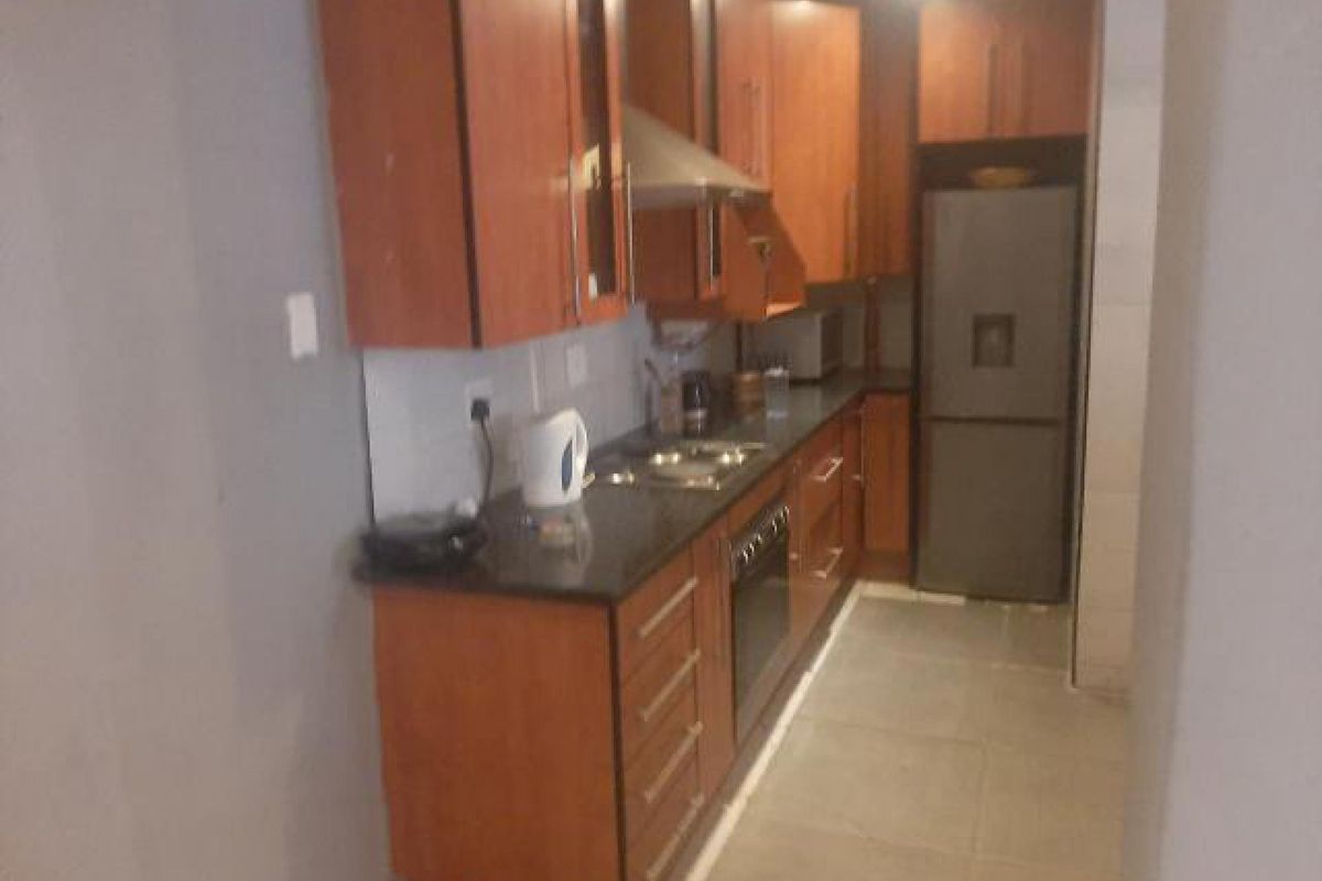 A compact kitchen featuring wooden cabinetry, stone countertops, built-in oven, hob, and extractor fan with tiled flooring.