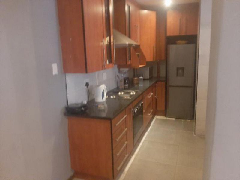 A compact kitchen featuring wooden cabinetry, stone countertops, built-in oven, hob, and extractor fan with tiled flooring.
