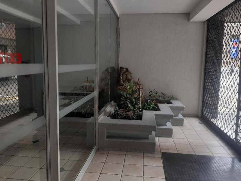 A clean apartment building entrance lobby featuring tiled flooring, large glass panels, and built-in concrete planters.