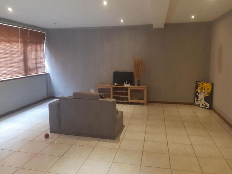 A spacious living area featuring neutral tiled flooring, recessed downlighting, and large windows fitted with venetian blinds.