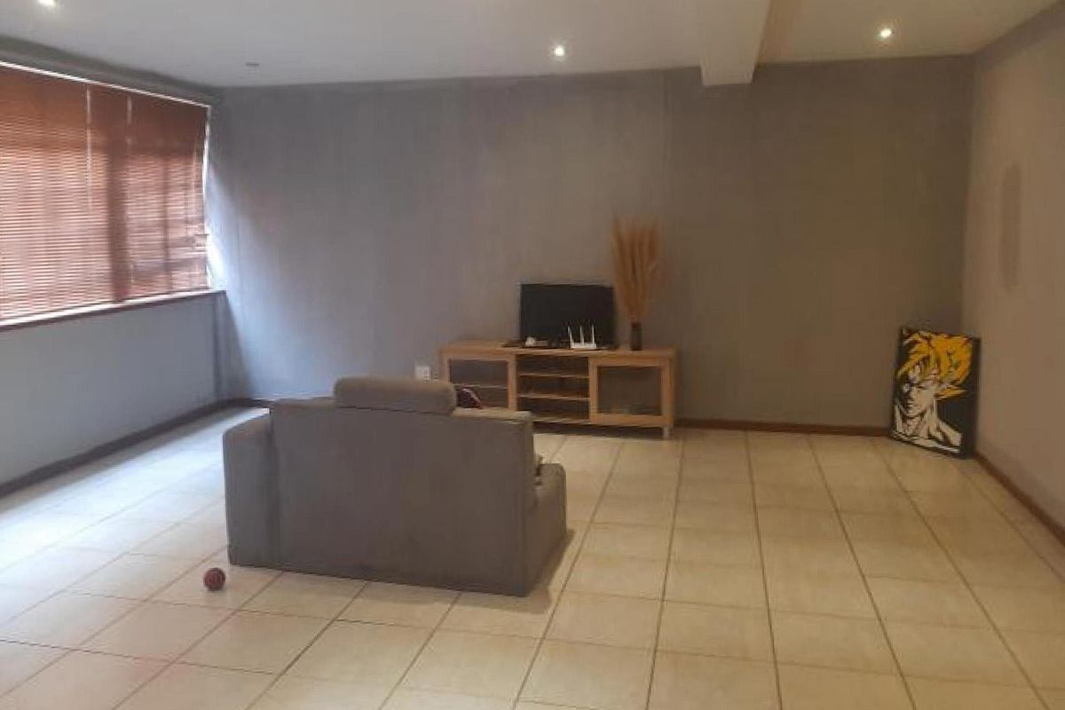 A spacious living area featuring neutral tiled flooring, recessed downlighting, and large windows fitted with venetian blinds.