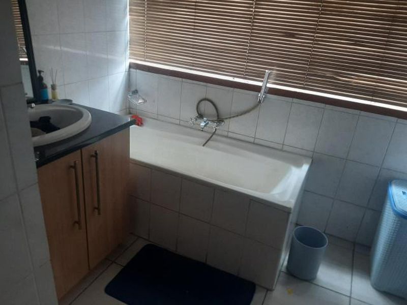 A functional bathroom featuring a tiled bathtub, built-in vanity cabinet, and wall-mounted shower fixtures, finished with neutral ceramic wall tiles.