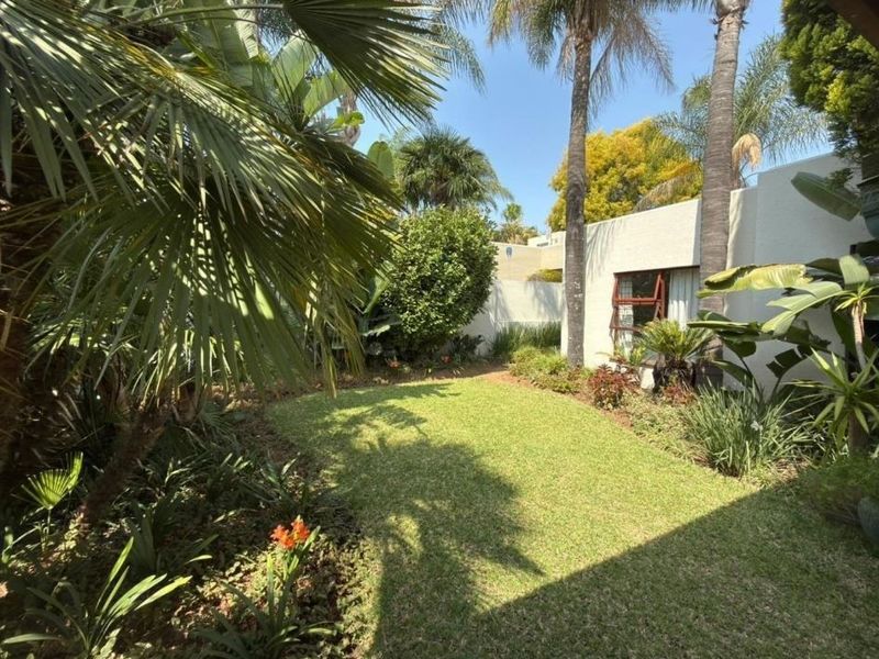 A well-maintained private garden featuring a lush green lawn, mature palm trees, and established perimeter walling.