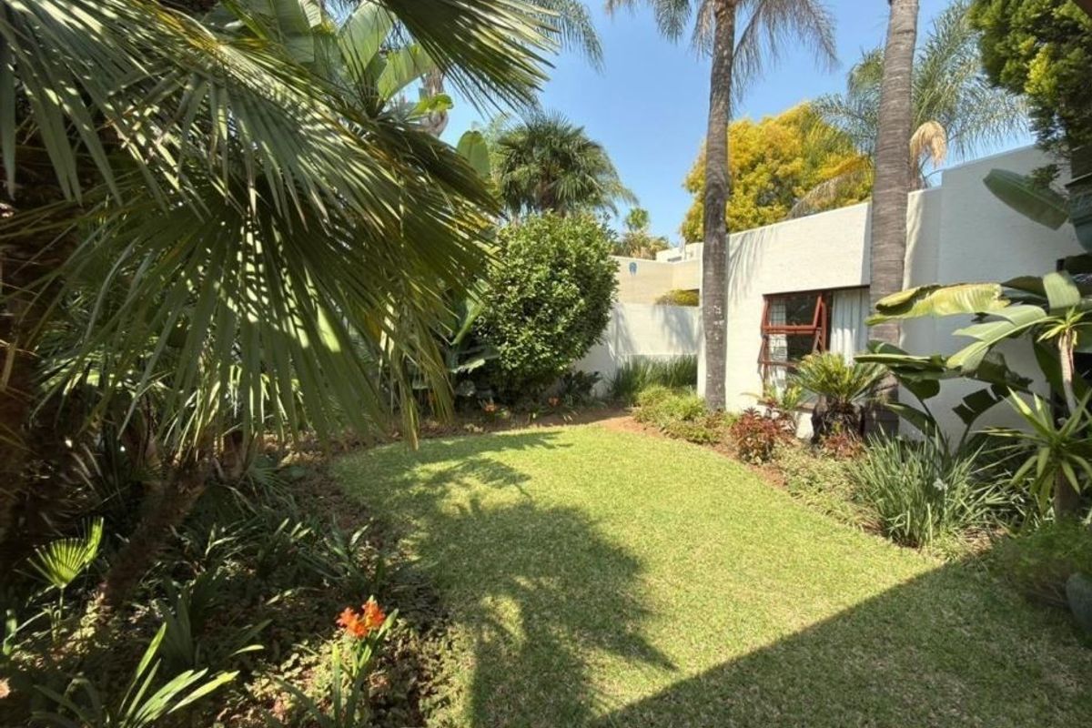 A well-maintained private garden featuring a lush green lawn, mature palm trees, and established perimeter walling.