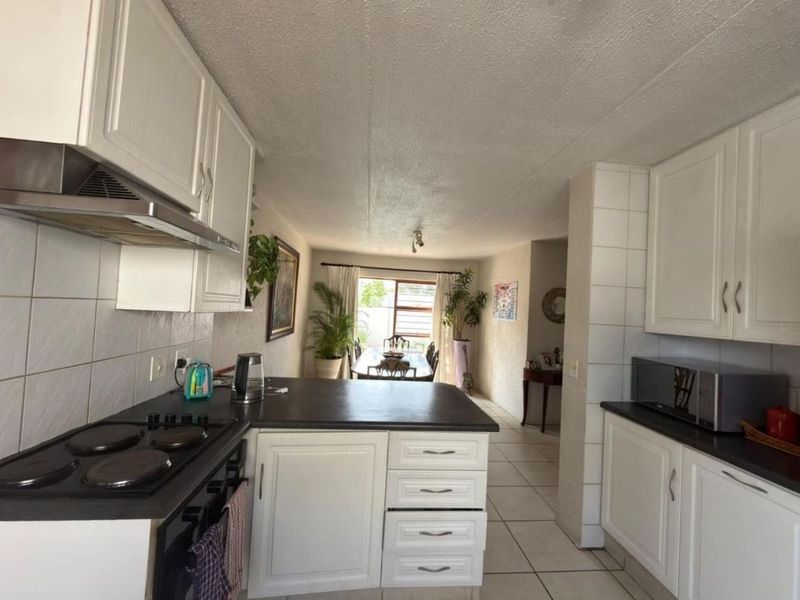 Open plan kitchen and dining area featuring white cabinetry, dark countertops, electric hob, extractor fan, and tiled flooring throughout.