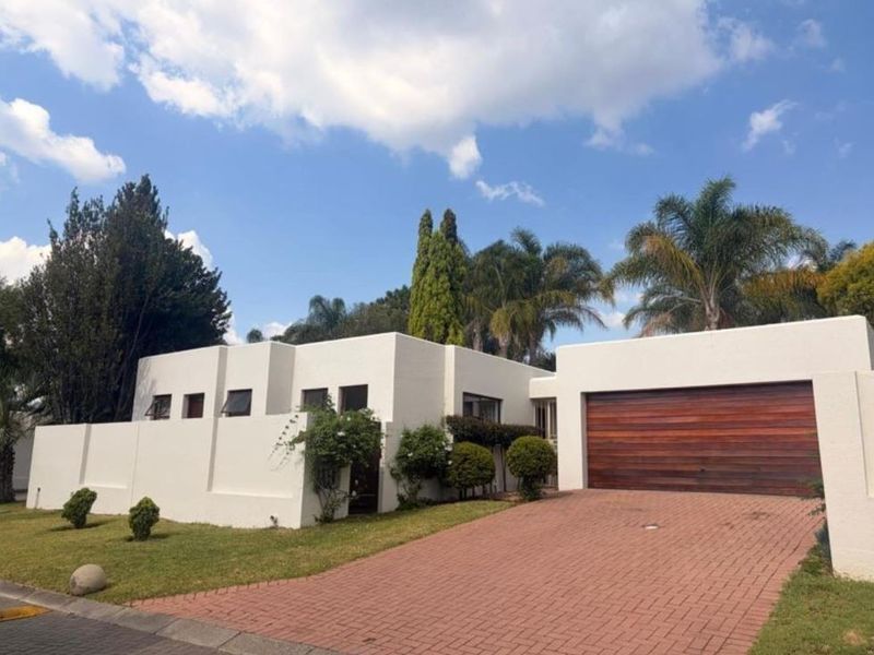 Front elevation of a modern house featuring a paved driveway, a prominent wooden garage door, and clean white exterior walls.