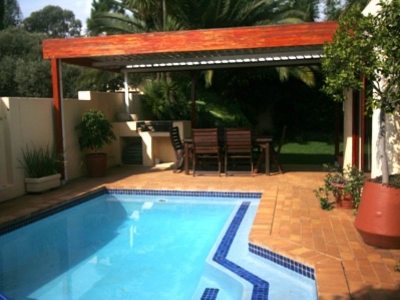 Outdoor pool area featuring a swimming pool, brick paving, and a covered patio with a built-in braai, perfect for entertaining.