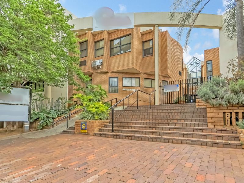 Front exterior view of a multi-story brick office building featuring a paved staircase entrance, metal security gate, and established landscaping.