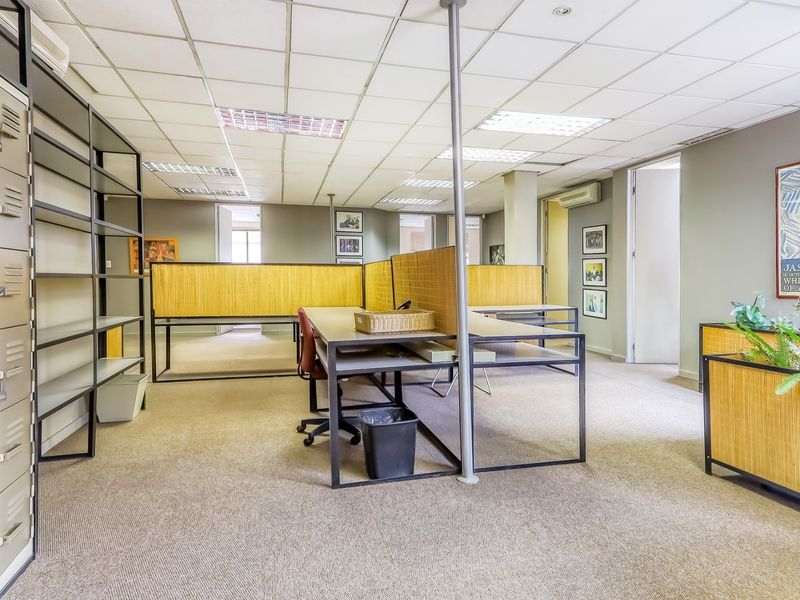 Open-plan office space featuring carpeted flooring, suspended ceilings with recessed lighting, built-in metal storage lockers, and partitioned workstation frames.