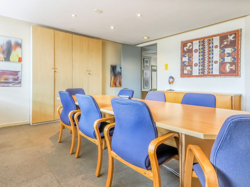 A professional office boardroom featuring built-in light wood cabinetry, recessed ceiling lighting, and carpeted flooring, suitable for meetings and collaborative work.
