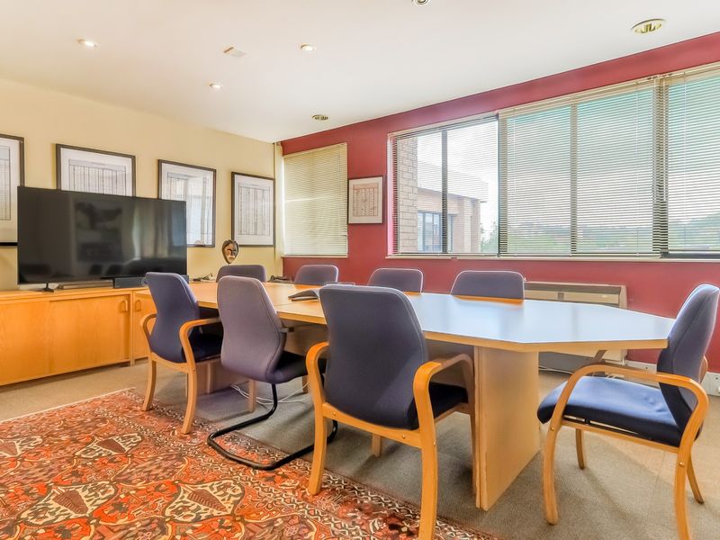 A functional office meeting room featuring built-in cabinetry, recessed lighting, and large windows with venetian blinds.