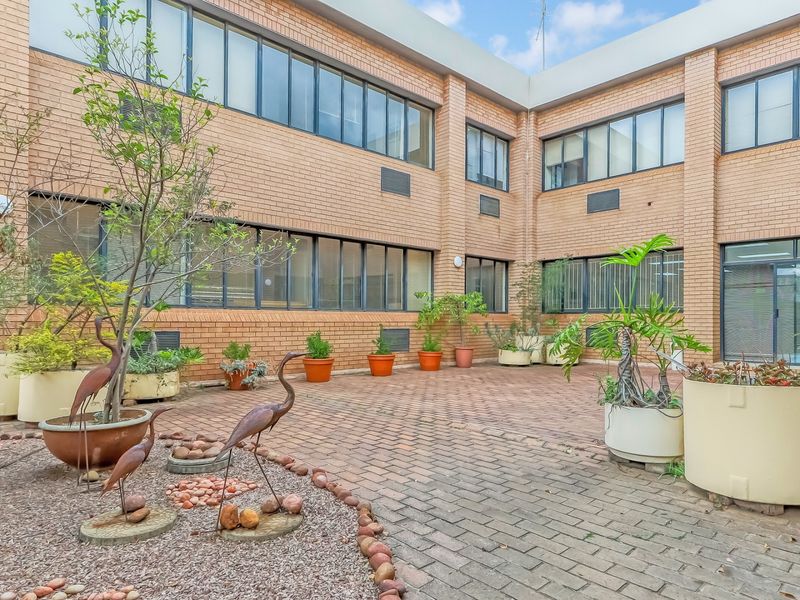 A paved rear courtyard area featuring a brick building facade with large windows and integrated air conditioning units.