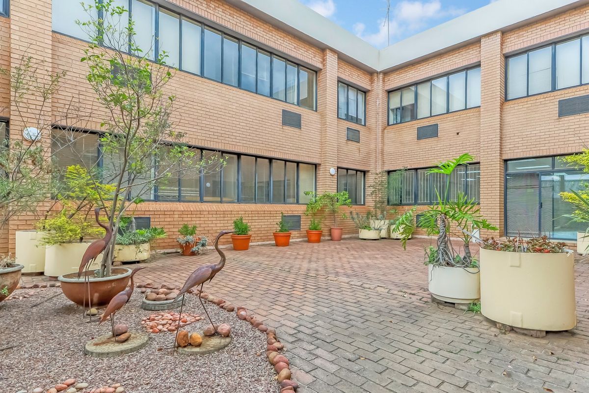 A paved rear courtyard area featuring a brick building facade with large windows and integrated air conditioning units.