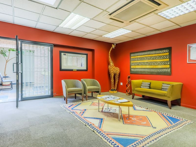 A bright office reception area featuring red walls, a suspended ceiling with integrated lighting, and a secure glass entrance door.