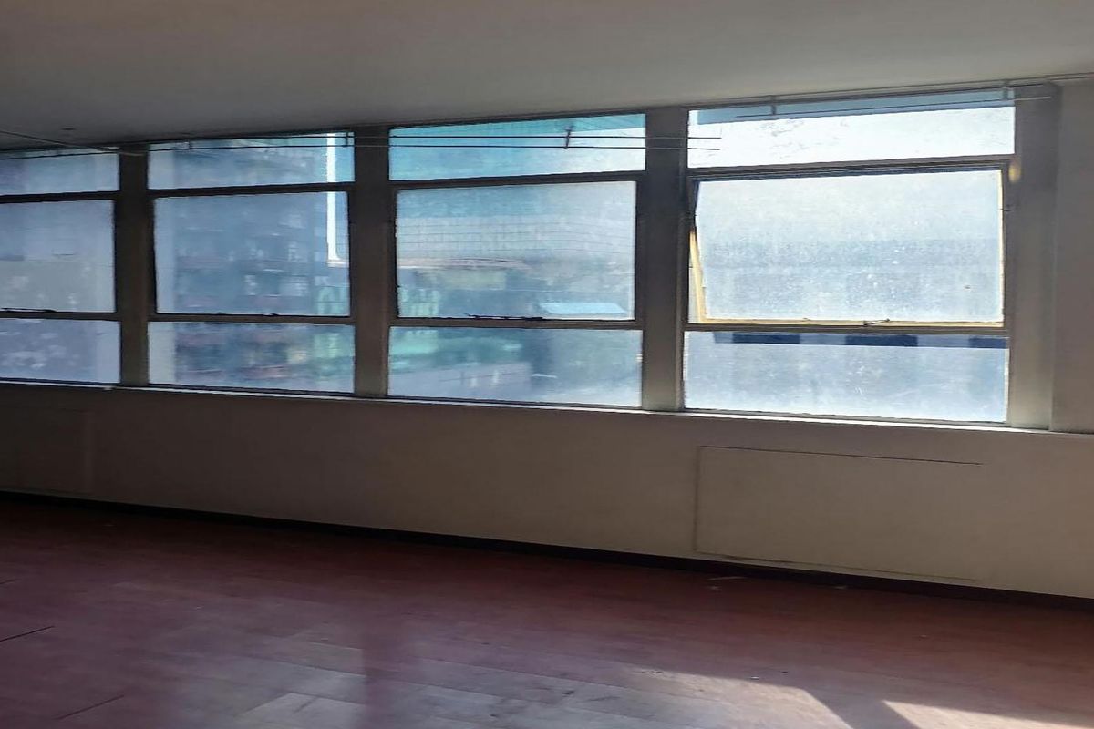 An empty living area featuring a large bank of windows providing ample natural light and laminate flooring throughout.
