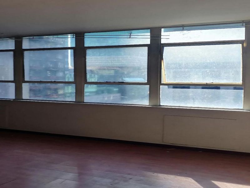 An empty living area featuring a large bank of windows providing ample natural light and laminate flooring throughout.