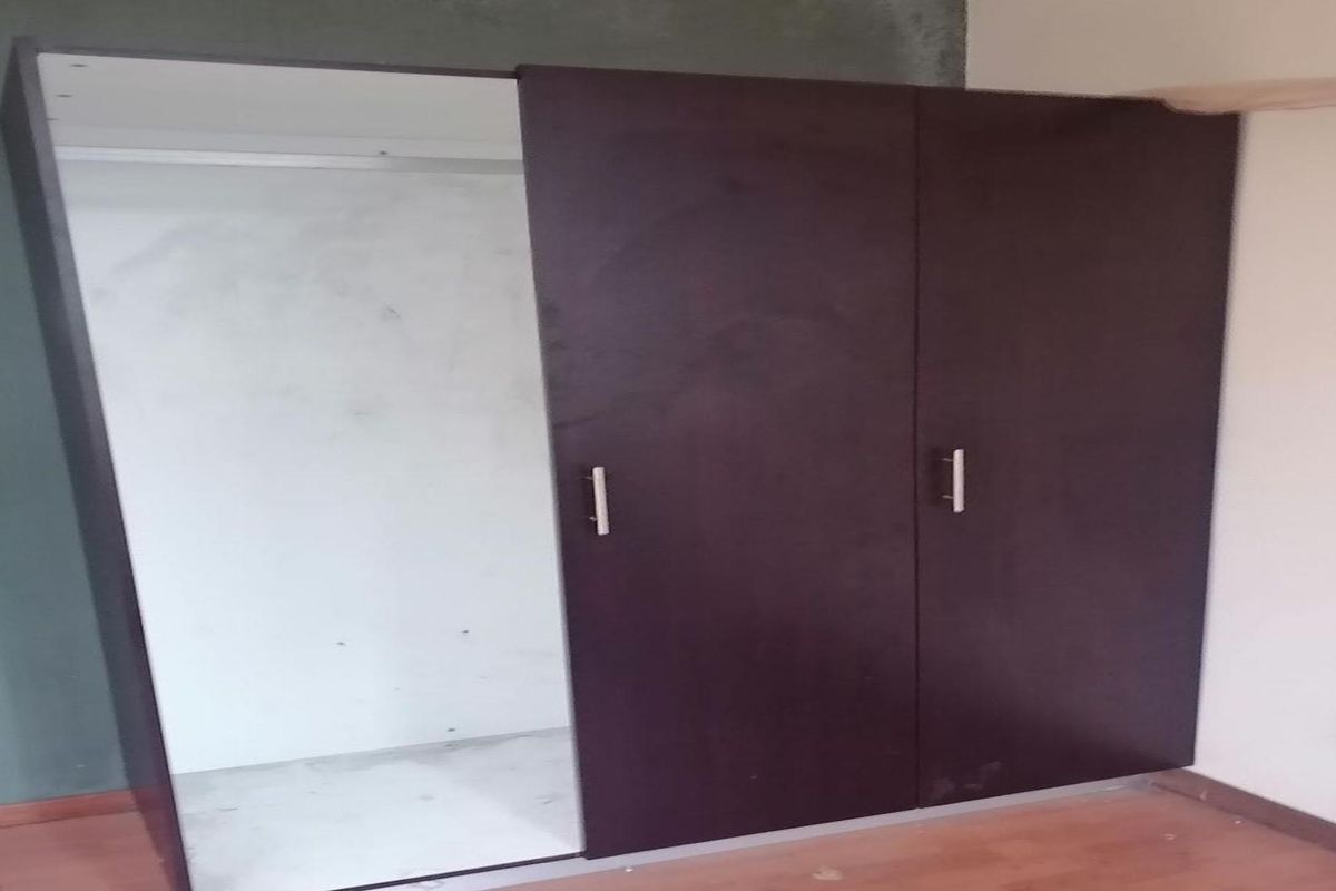 A bedroom featuring a built-in wardrobe with sliding doors, laminate flooring, and an electrical outlet, requiring minor cosmetic finishing to the surrounding walls.