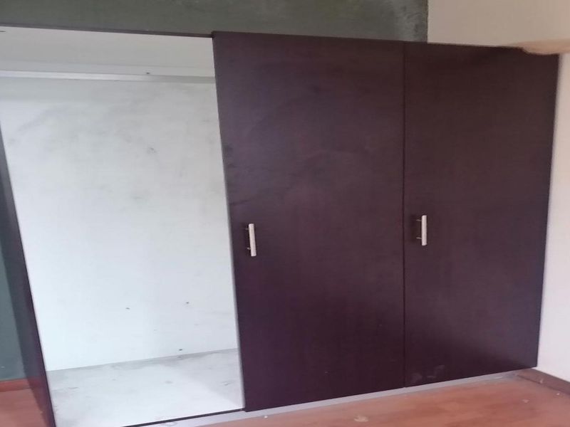 A bedroom featuring a built-in wardrobe with sliding doors, laminate flooring, and an electrical outlet, requiring minor cosmetic finishing to the surrounding walls.