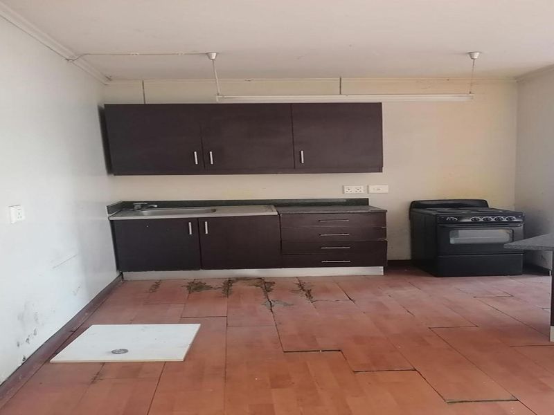 A basic kitchen area featuring dark cabinetry, a stainless steel sink, and a freestanding stove, requiring significant maintenance and flooring repairs.