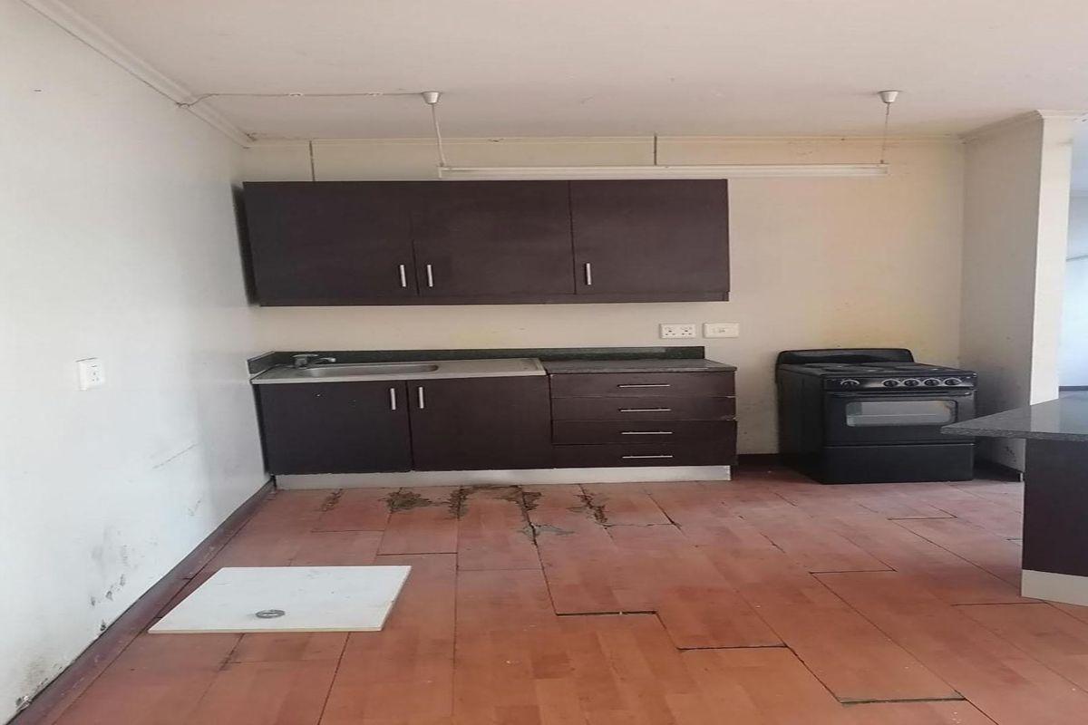 A basic kitchen area featuring dark cabinetry, a stainless steel sink, and a freestanding stove, requiring significant maintenance and flooring repairs.